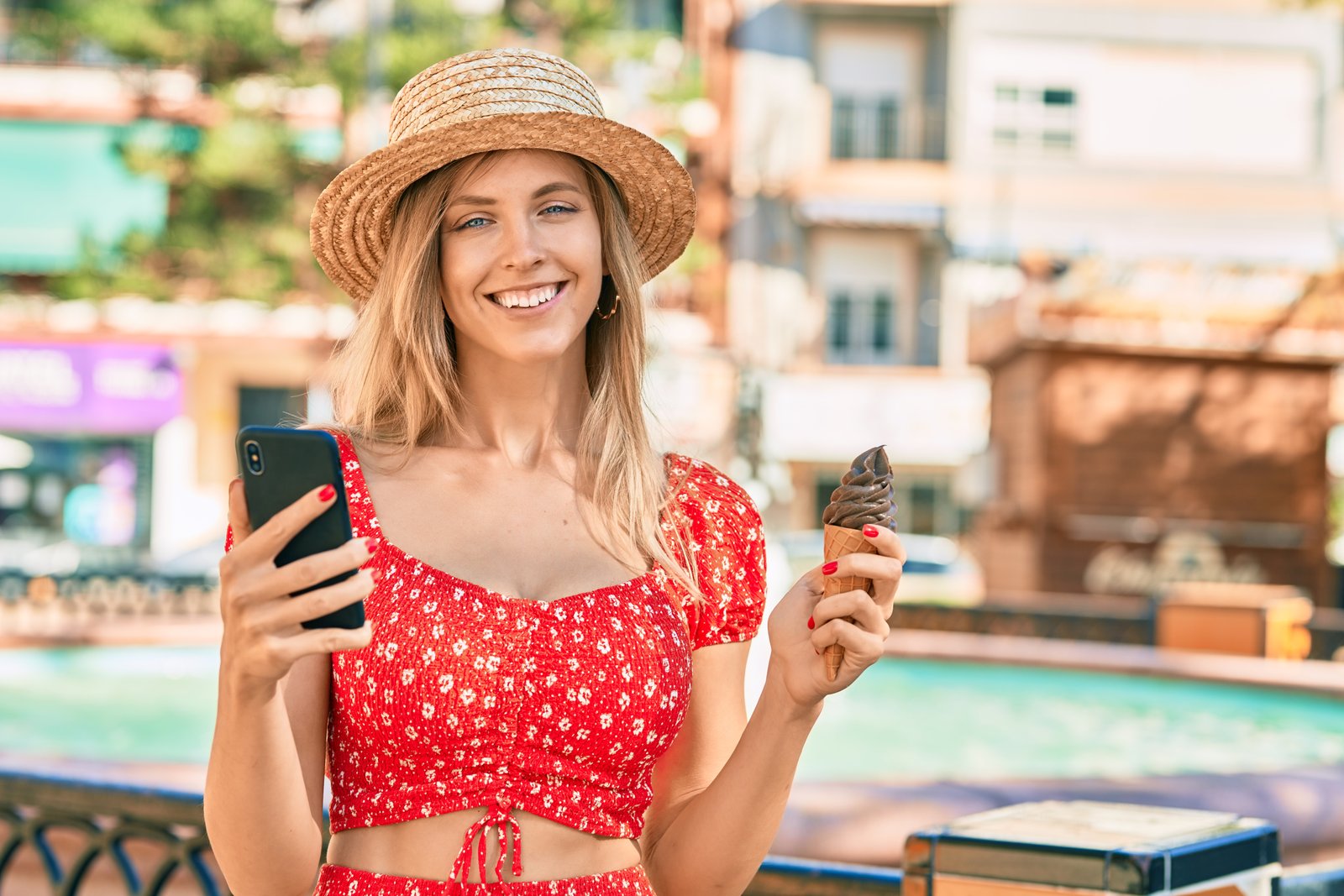 Young blonde tourist woman wearing summer style using smartphone eating ice cream at the city.